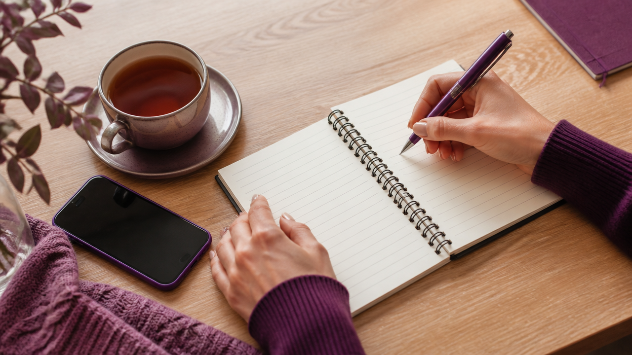 Mãos escrevendo perguntas em um caderno ao lado de chá e celular antes de uma consulta online