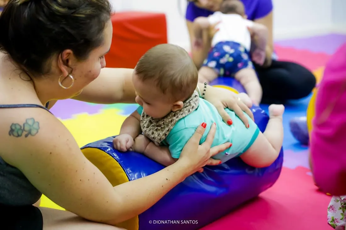 Mãe auxilia bebê em atividade psicomotora sobre rolo colorido durante aula para bebês da Baby Gym Manaus