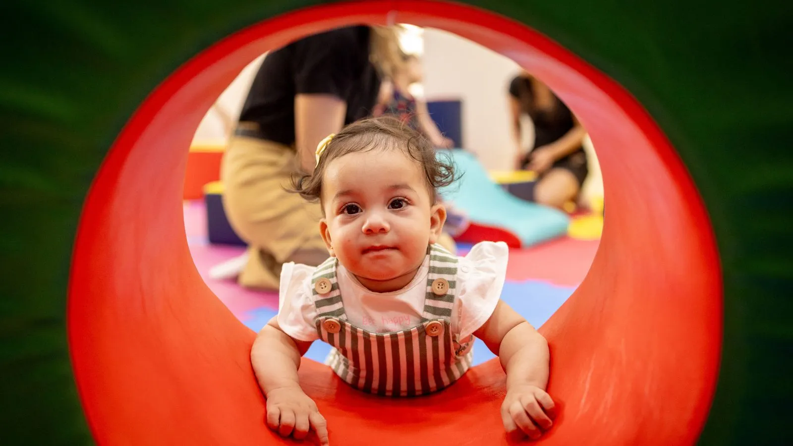 Bebê engatinha por um túnel colorido durante atividade na Baby Gym Manaus.