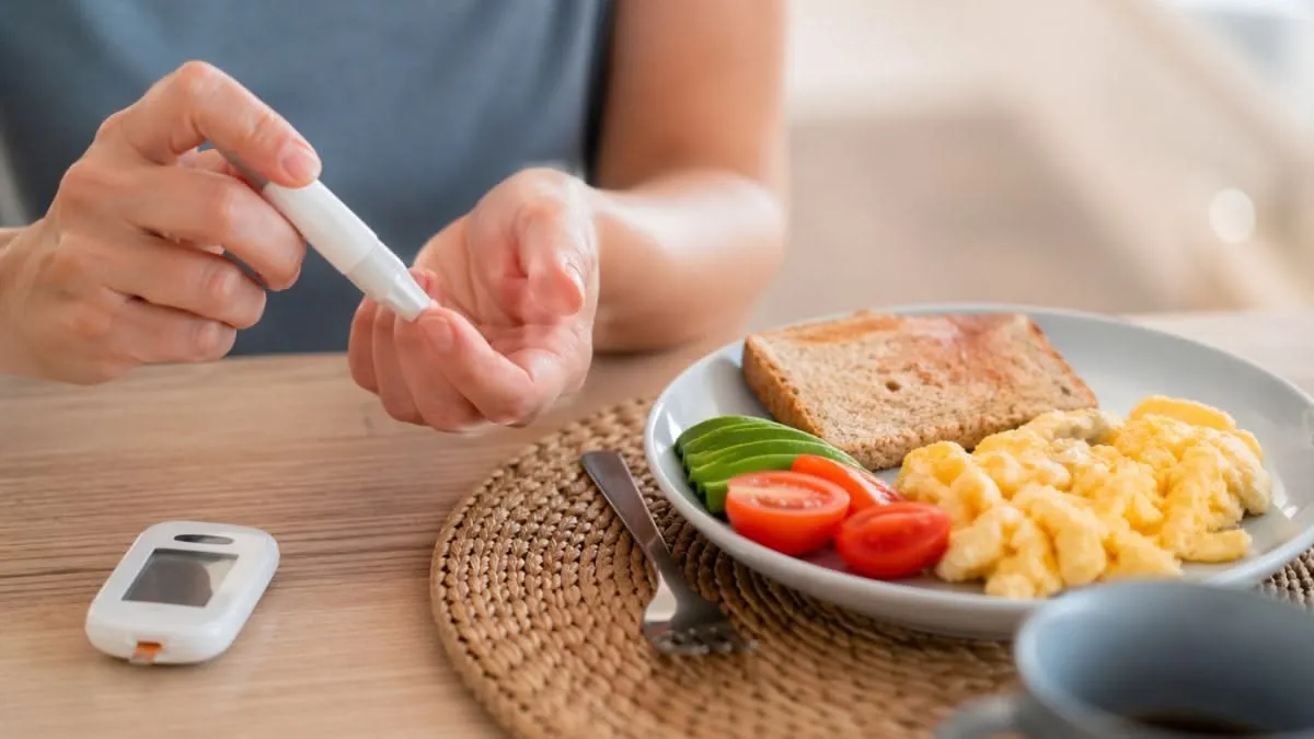 Mulher fazendo a conferência de sua glicose, prestes a se alimentar. EM cima da mesa um prato com uma refeição equilibrada e um glicosímetro